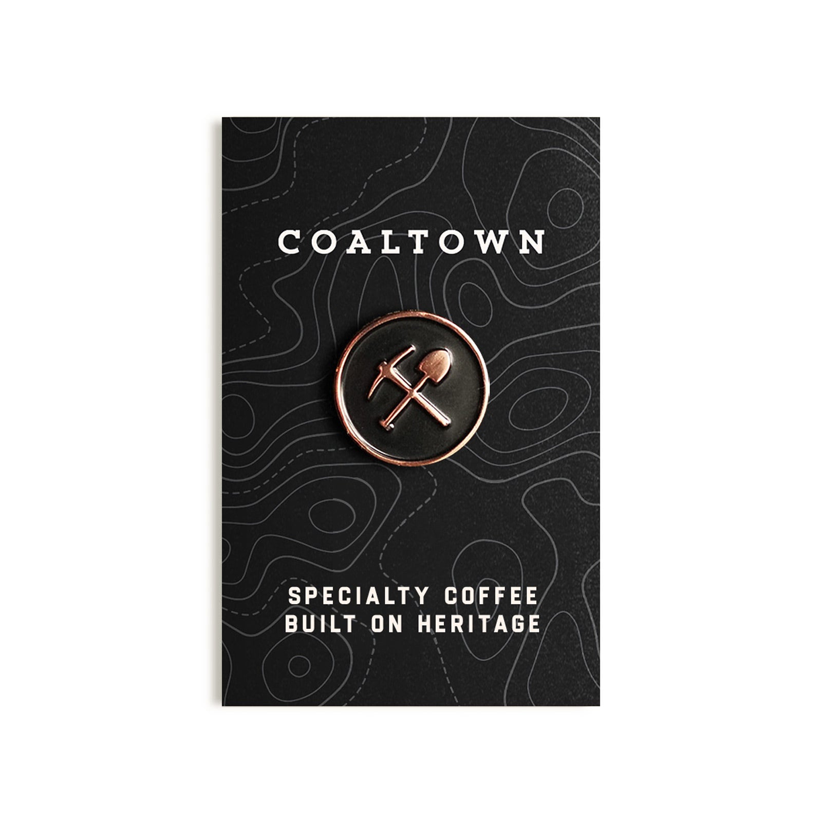 A polished stamped copper pin with black enamel inlay, displayed on a card with 'COALTOWN' and 'SPECIALTY COFFEE BUILT ON HERITAGE' printed on it.