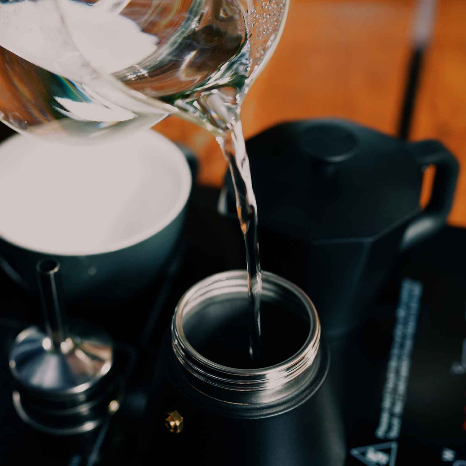 Coffee being poured from a glass carafe into a black moka pot.