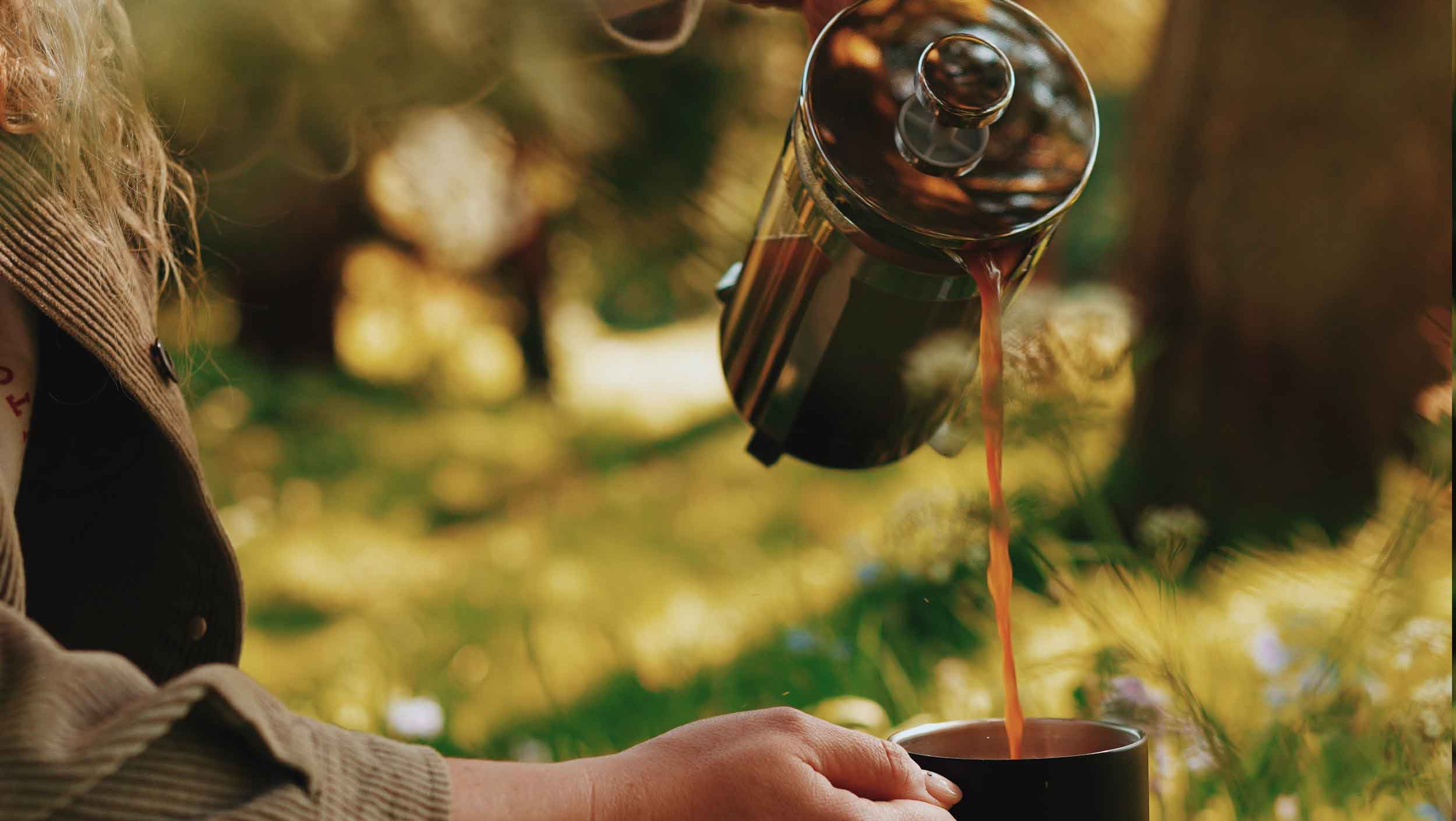 Pouring a french press coffee into a keep cup in a park