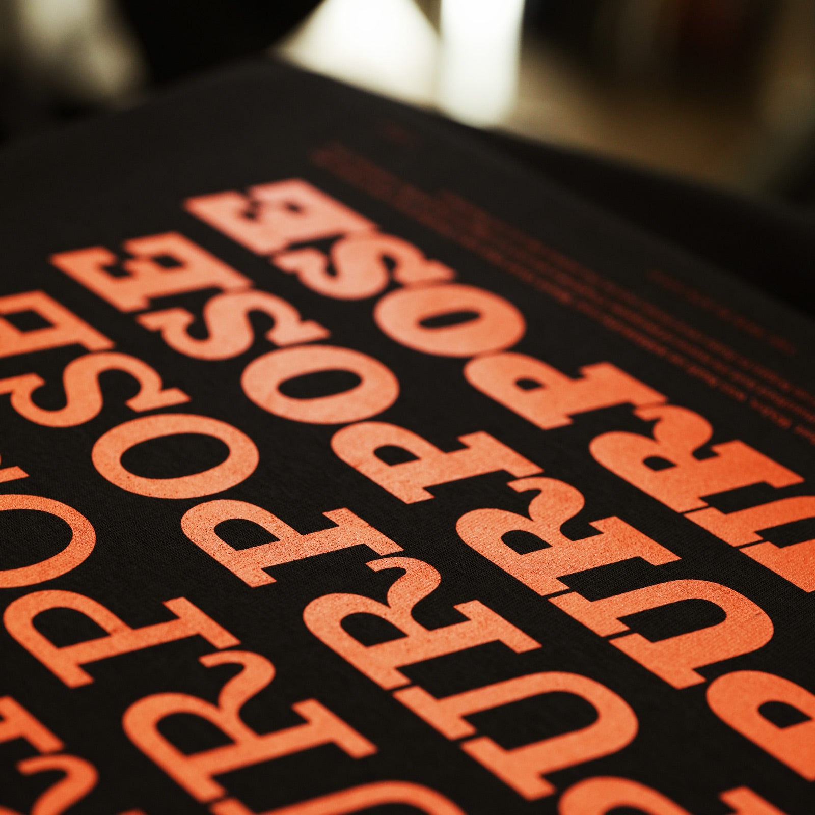 A close-up shot of a black printed sheet featuring the word 'PURPOSE' repeated in large, bold orange letters, photographed with a shallow depth of field.