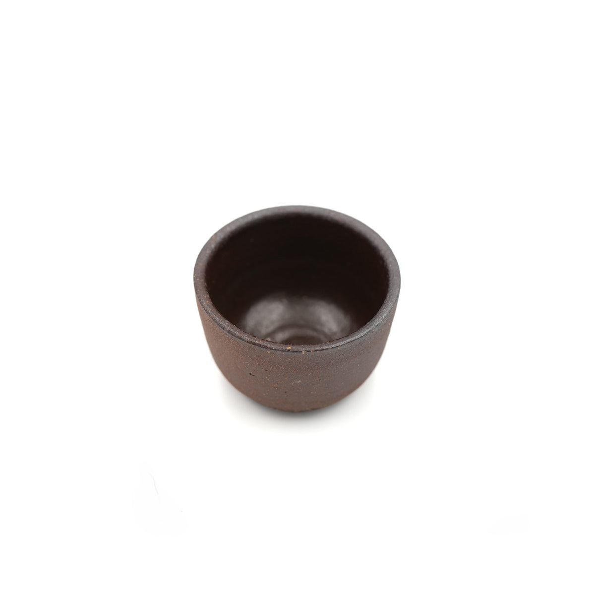 A small, dark brown ceramic cup with a textured matte finish, photographed from a top-down perspective on a solid white background.