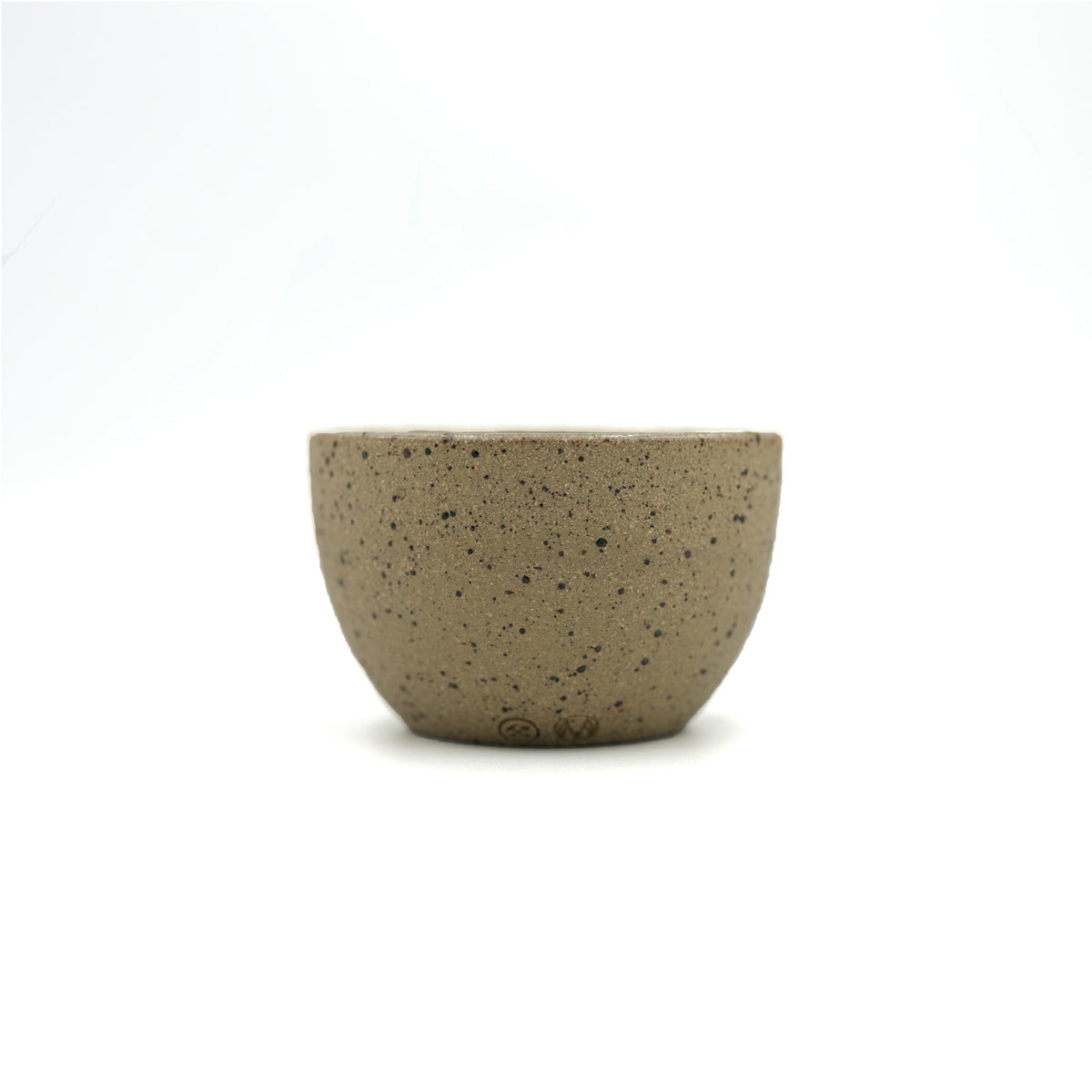 A small, round ceramic cup with a speckled beige and brown glaze, photographed against a seamless white background.