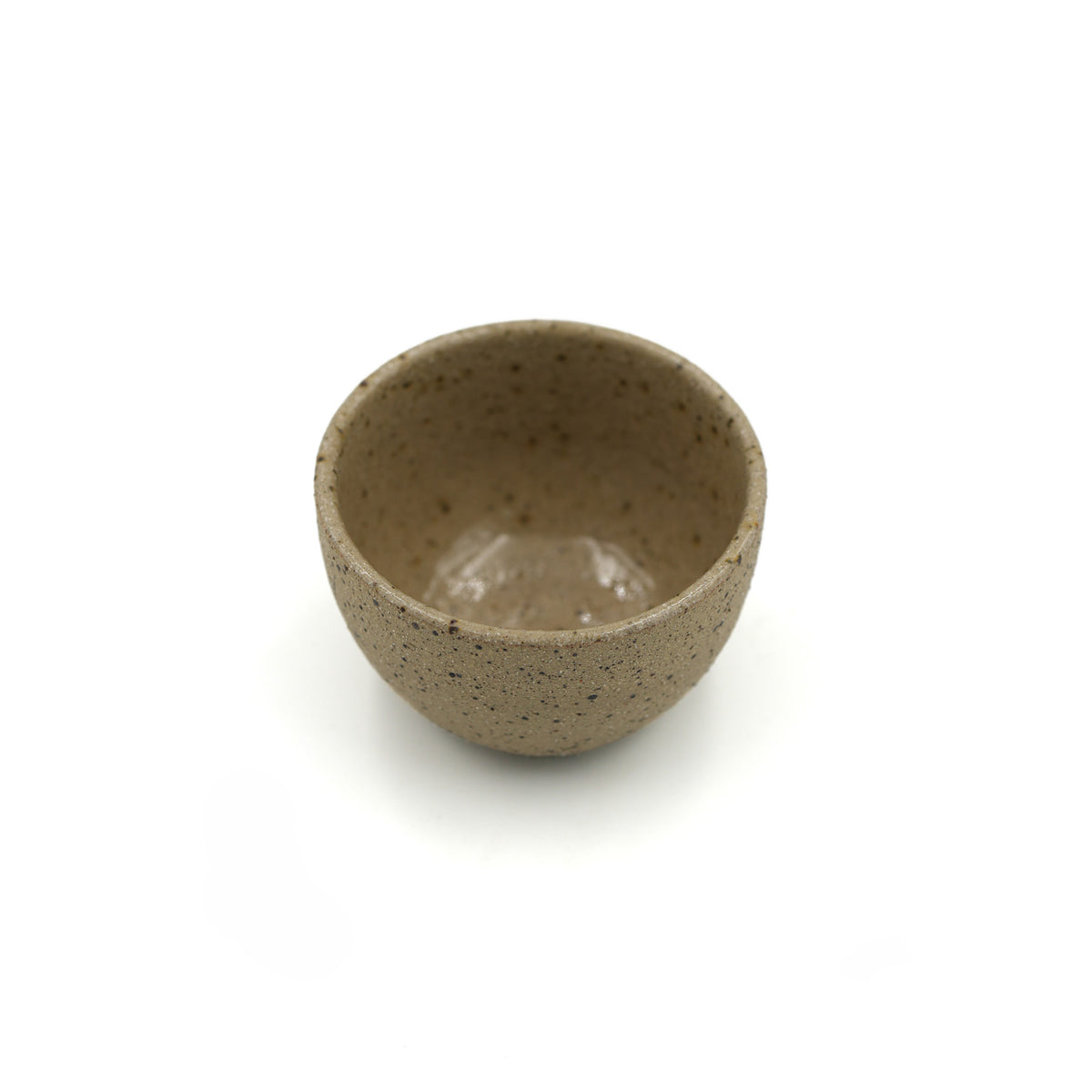 A small handmade ceramic cup with a speckled beige and brown glaze, shown from a top-down view on a white background.