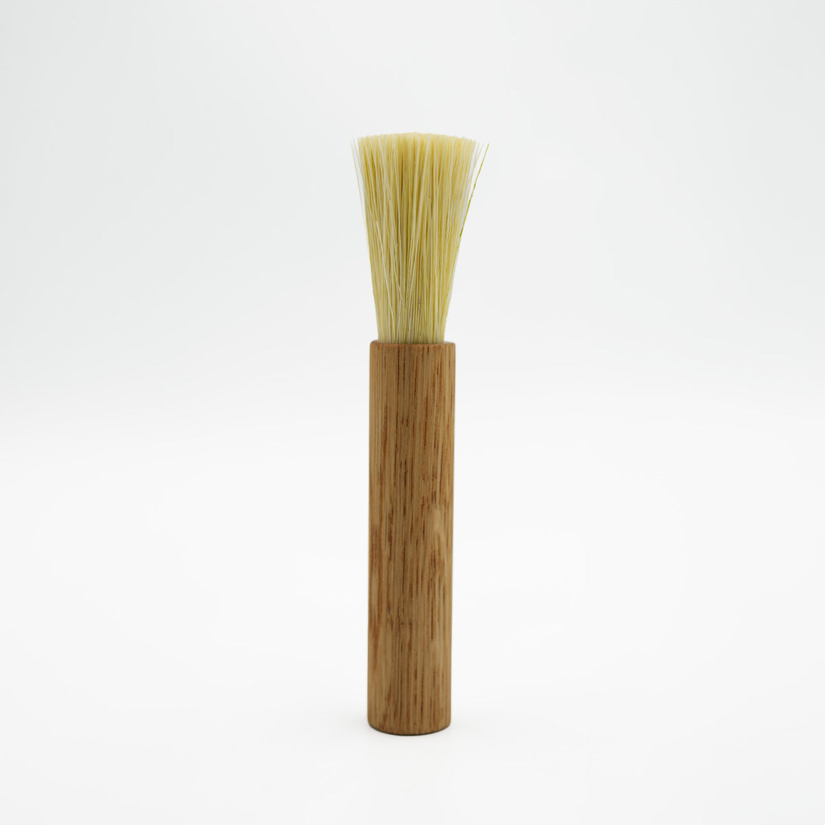 A traditional Japanese coffee brush with a light brown wooden handle and natural beige bristles, standing upright against a seamless white background.
