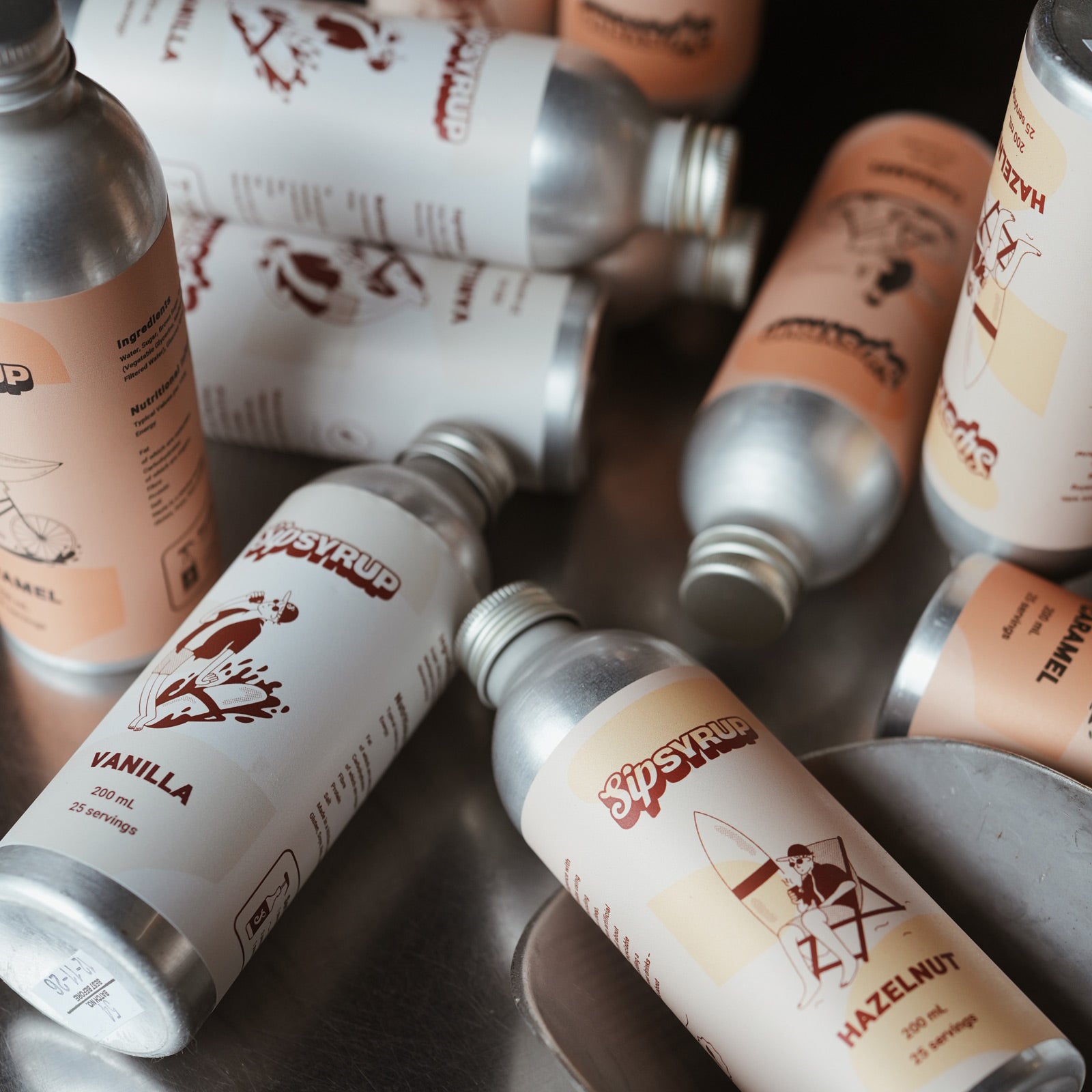 Several silver metal bottles of Sip Syrup with white labels written vanilla, hazelnut and caramel. 