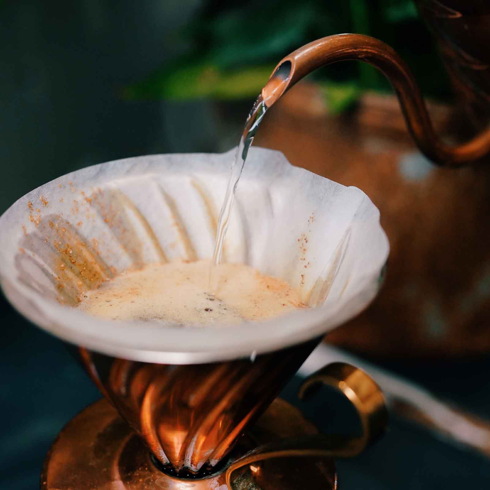 Copper coffee dripper and V60, with paper filter and water being poured into it.